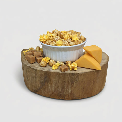 Wooden platter with bowl of popcorn, cheese, and crackers on a light gray background
