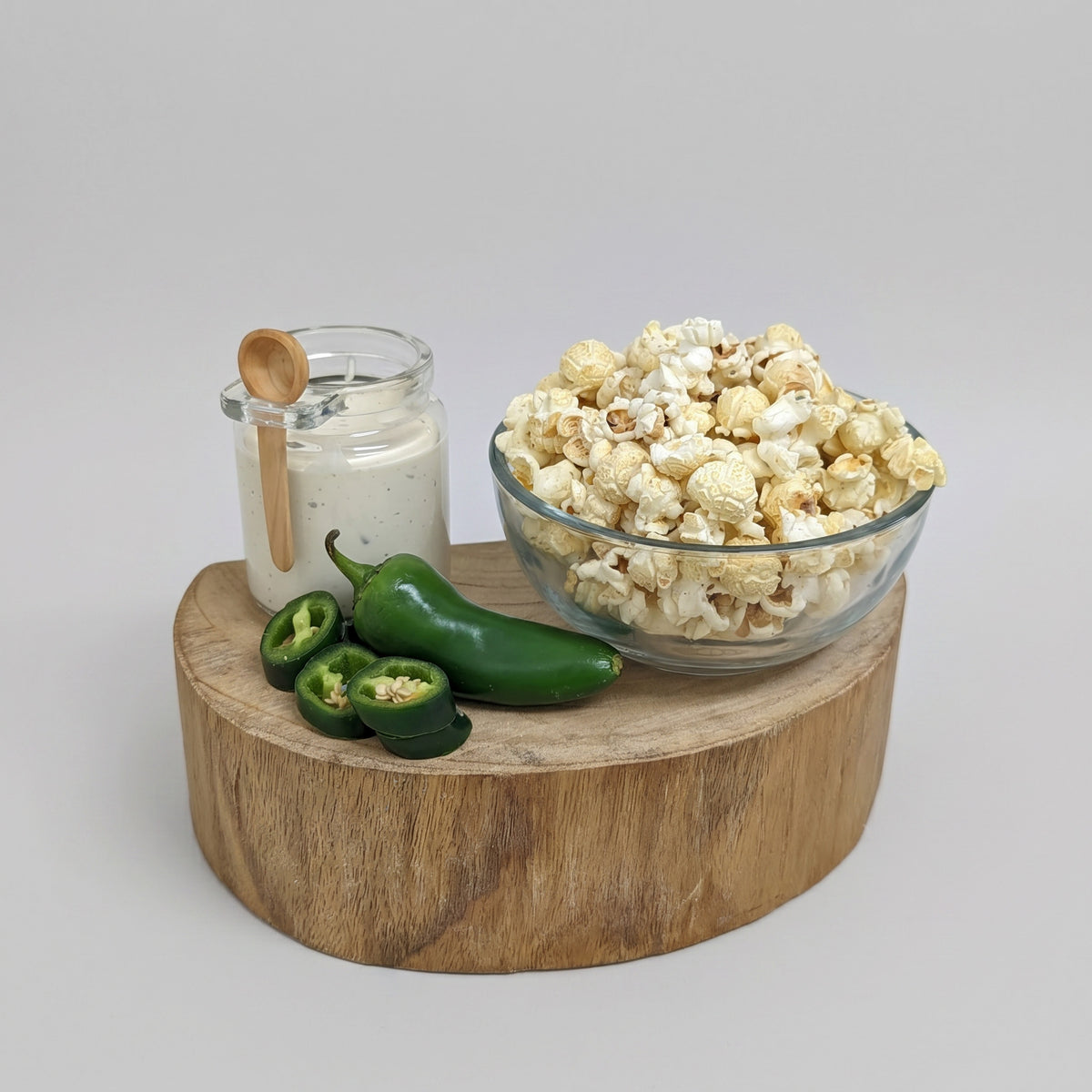 Clear glass bowl of popcorn on a wooden board with jalapeños and a jar of ranch dressing.