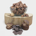 Glass bowl of chocolate-covered nuts on a wooden block with chocolate candies and cookies.