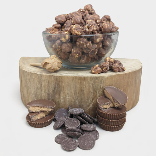 Glass bowl of chocolate-covered nuts on a wooden block with chocolate candies and cookies.