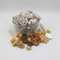 Assorted snack mix including pretzels, popcorn, and chocolate pieces on a light gray background.