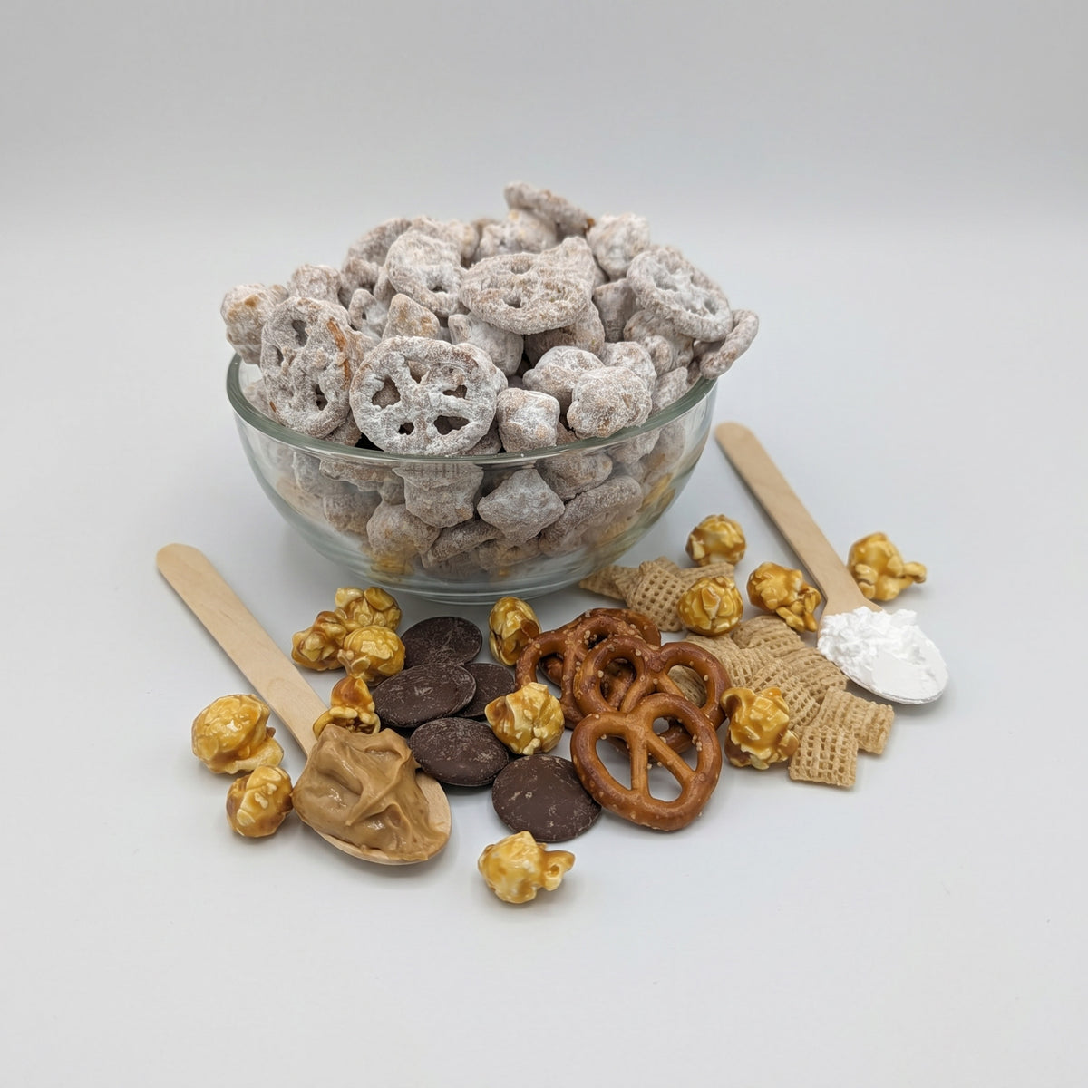 Assorted snack mix including pretzels, popcorn, and chocolate pieces on a light gray background.