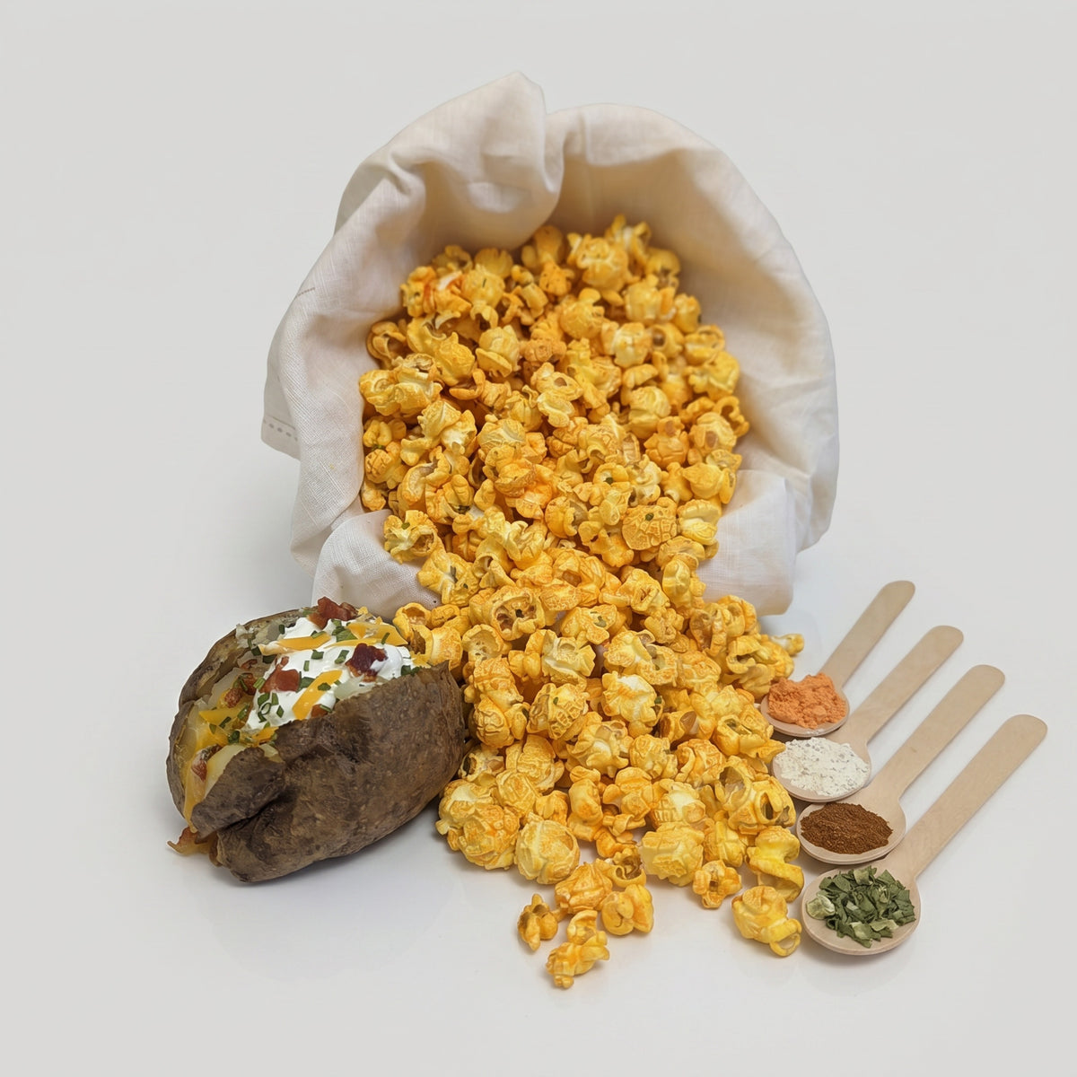 Bag of popcorn with a baked potato and wooden spoons with seasonings on a white background