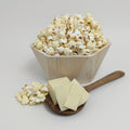 Wooden bowl filled with popcorn and a wooden spoon with cheese slices on a light gray background