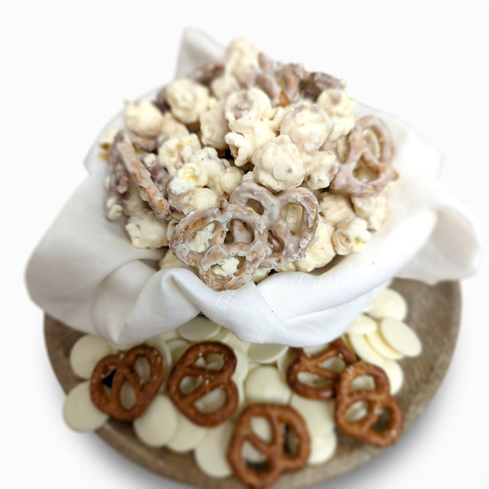 Assorted snack mix with pretzels and popcorn in a white bowl on a white background