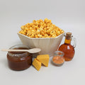 Wooden bowl of popcorn with caramel sauce, cheese, and a bottle on a white background