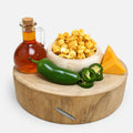 Wooden board with popcorn, cheese, jalapeños, and a bottle of syrup on a white background