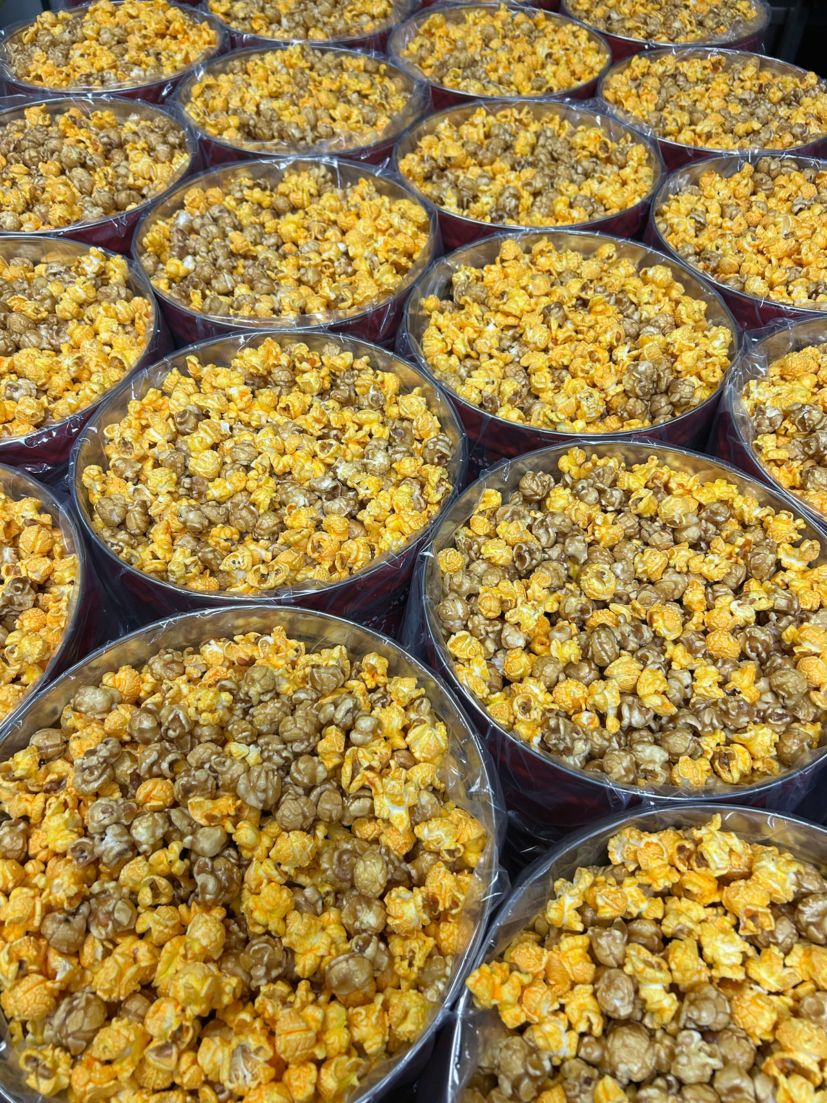 Multiple clear plastic cups filled with yellow and golden popcorn kernels arranged closely together.
