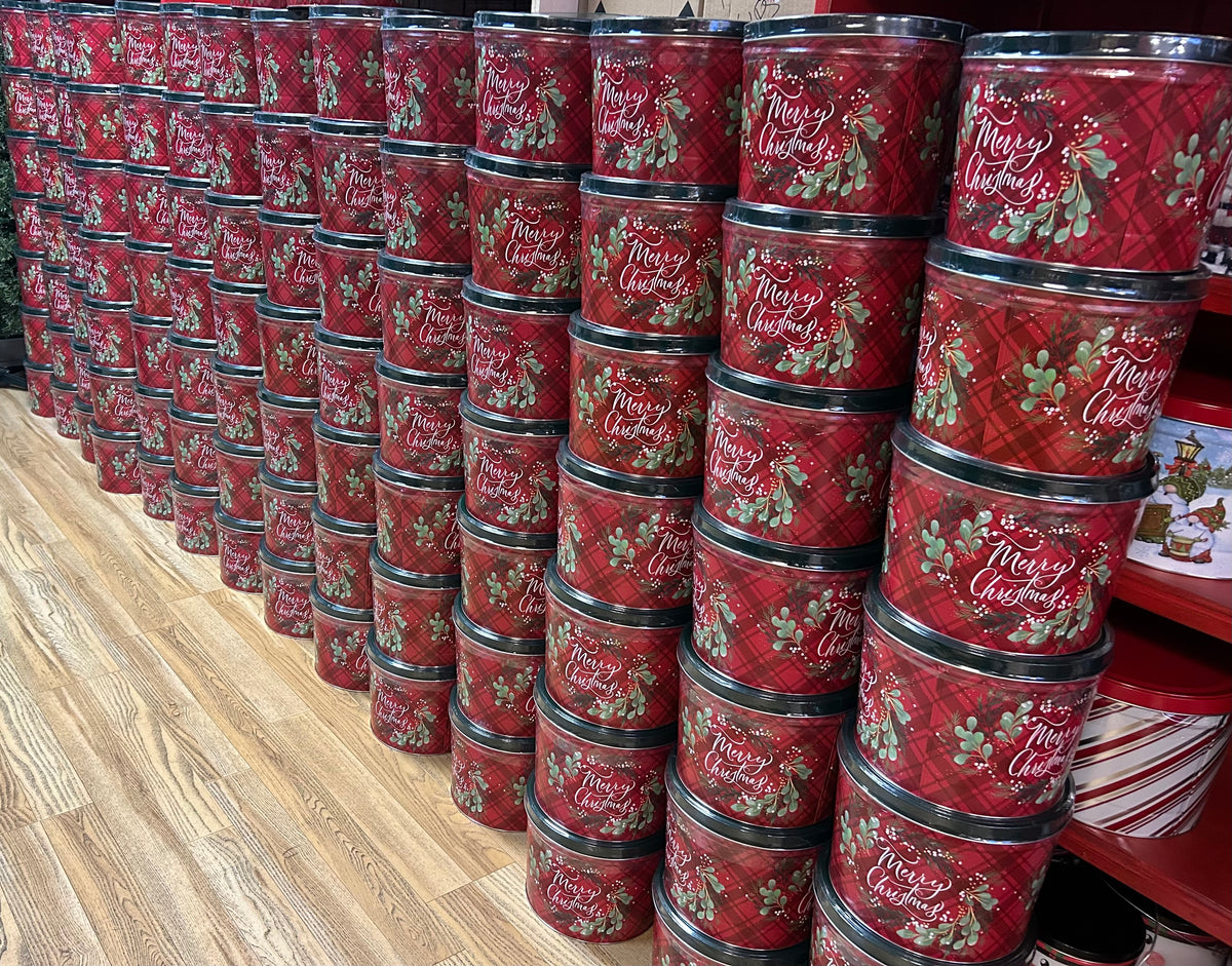 Stacked red Christmas gift tins with plaid patterns, holly leaves, and Merry Christmas text on metal lids