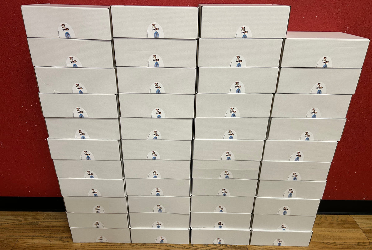 A stack of white shoe boxes arranged in a grid against a dark red wall and light wood floor. Each box has a small printed label near the top showing a figure in a blue suit.