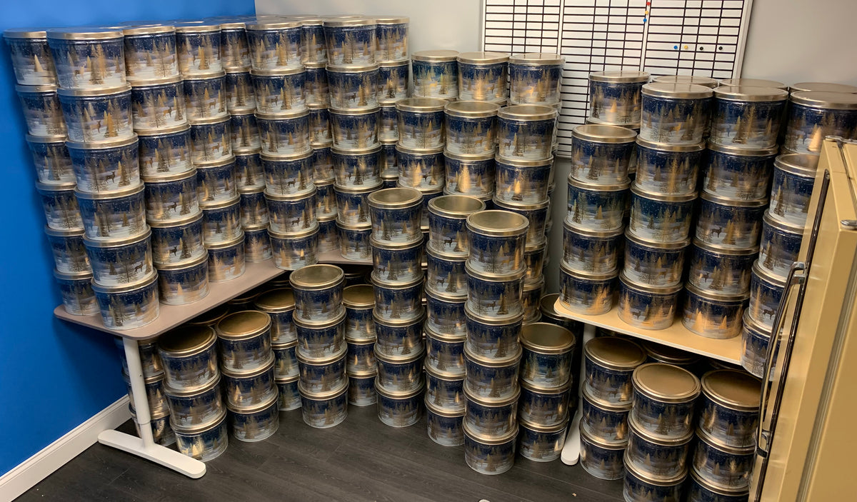 Thousands of paint cans stacked in rows on tables and the floor in a storage room with blue walls.