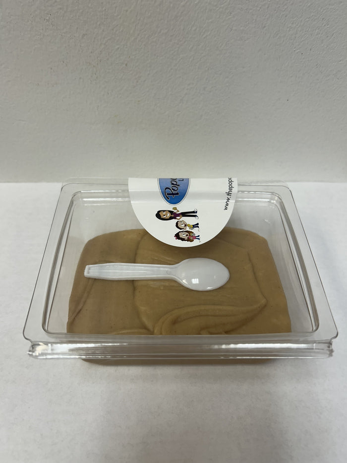 A clear plastic clamshell package containing peanut butter fudge, with a small white plastic spoon resting on top and a white label sticker at the front.