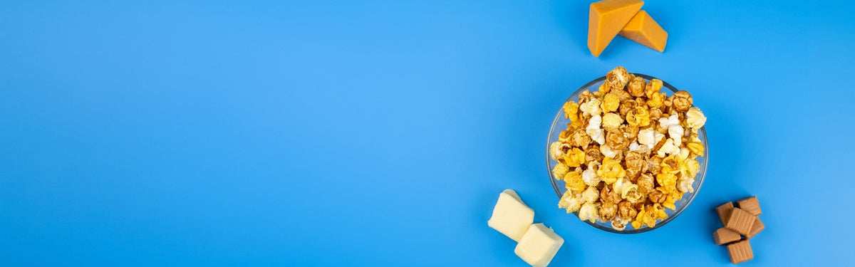 Bowl of popcorn with caramel and white pieces, plus butter cubes and chocolate squares on a blue background