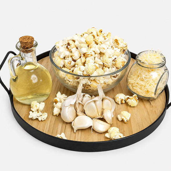 Wooden tray with popcorn, garlic bulbs, and a bottle of oil on a white background